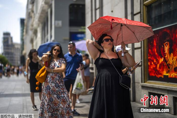 2022年7月18日，西班牙马德里，一名妇女在炎热的阳光下撑伞遮阳。